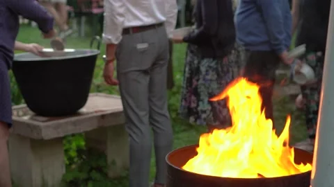 Fire burning in a barrel with people getting food in the background Stock Footage 232760273