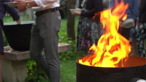 Fire burning in a barrel with people getting food in the background Video stock 232760277