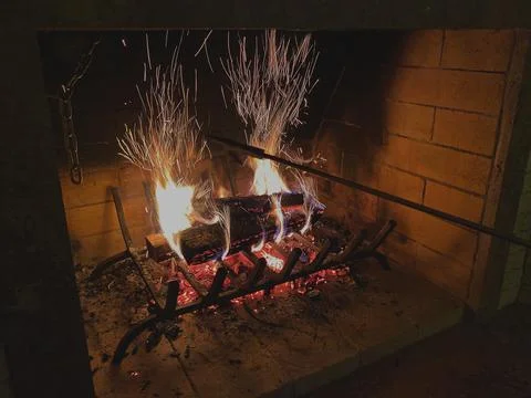 Fire is burning in the fireplace. The hand throws wood into the burning hearth 库存照片