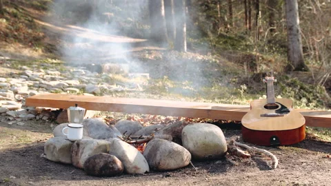 Fire is burning in the forest, there is smoke, and a guitar is lying next to it Stock Footage 195205176