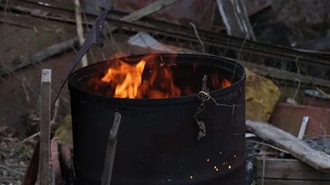 A fire burning inside an old rusty barrel outdoors Stock Footage 182801114