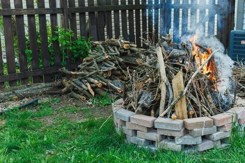 Fire burns in a backyard while piles of branches rest nearby in the early e.. Stock Photos