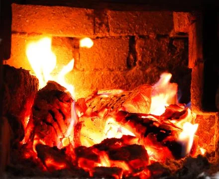 Fire burns in a brick fireplace during the evening hours creating warmth and Stock Photos