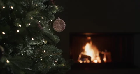 A fire burns in a fireplace in a dark room. Blurred Christmas tree lights in the Stock Footage 249605271