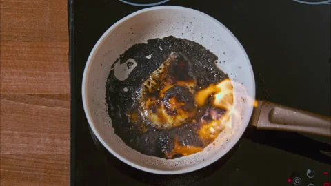Fire burns in a pan. burnt egg on a white pan in black oil on a black stove. 스톡 동영상 196501698