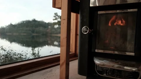 The fire burns in the sauna stove with panoramic windows sill to the lake Stock Footage 231143155