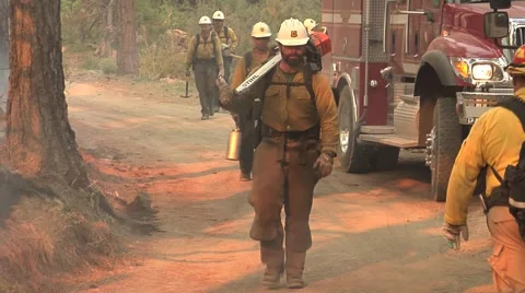 Fire crew walking up mountain road with chain saw and tools and firetrucks Stock Footage 40954151
