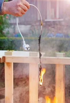 Fire on an electric wire with a plug in the hands of a man. Stock Photos