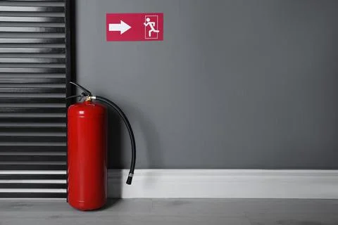 Fire extinguisher and emergency exit sign indoors. Space for text Stock Photos