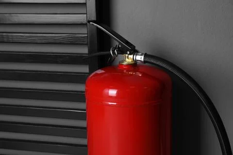Fire extinguisher near grey wall indoors, closeup Stock Photos