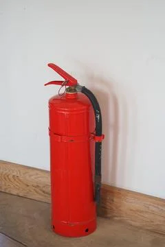 Fire extinguisher placed against a wall in a room with wooden flooring Stock Photos