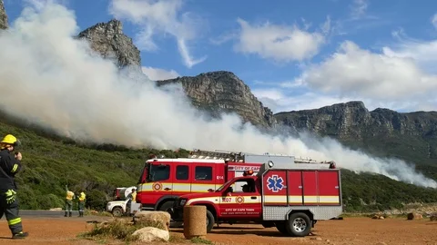 Fire fighter with hand held radio, fire fighting vehicles and mountain skyline Vídeo Stock 80988971