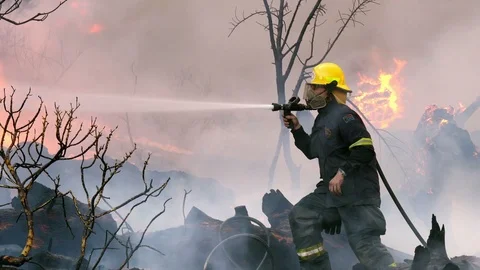 Fire fighter in yellow hat with sprays water near red flames Stock Footage