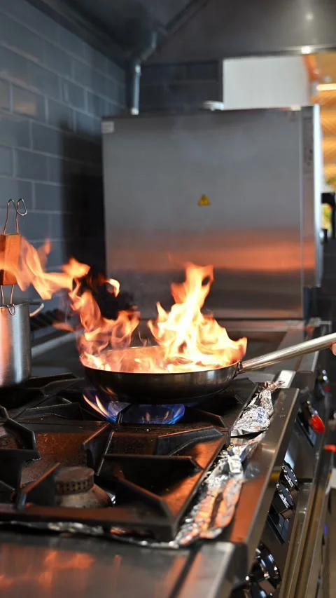Fire flare in a pan as a professional chef cooks on a commercial gas stove .. Stock Footage 338052748
