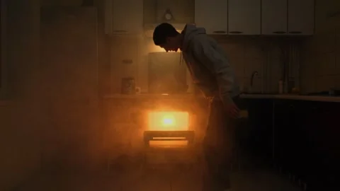 A fire-hazardous situation in the kitchen as a man pulls a burnt dish from the Stock Footage 305257712