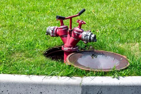 Fire hydrant connected to an open manhole on a green lawn with grass. Stock Photos