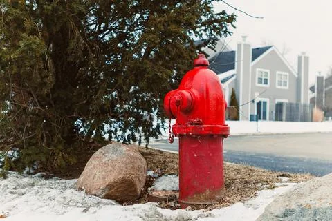 A fire hydrant is placed next to some rocks and snow in a residential area. H Stock Photos