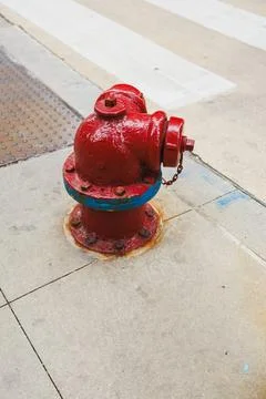 A fire hydrant is placed on the sidewalk close to a crosswalk. It has bright  Stock-Fotos