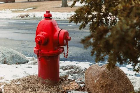 Fire hydrant stands on snow-covered ground near a rocky area on a winter da.. Stock Photos