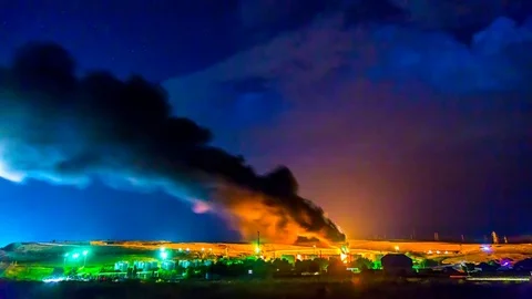 Fire at an oil refinery, at night during a thunderstorm. Strong burning of oil w Stock Footage 77714301