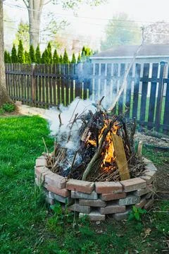 Fire pit with burning wood in backyard with colorful fence Stock Photos