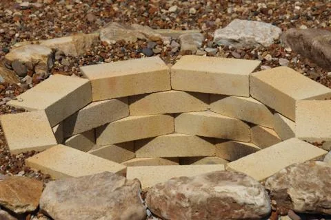 Fire pit made of the yellow aluminous bricks and boulders surrounded by peb.. Stock Photos