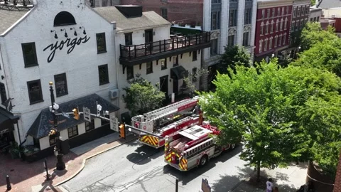 Fire truck idles at intersection beneath Yorgos signage, historic brick Stock Footage 338408646