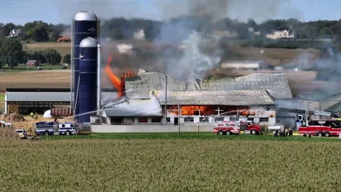 Fire Trucks parking in front of burning barn and farmstead at sunny day in USA Stock Footage 319809668
