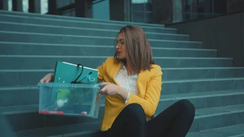 Fired young lady sitting down on stairway with office box items feel exhausted Video stock 129739184