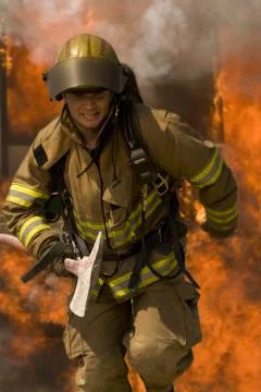 Firefighter with axe running from blaze Foto stock