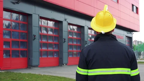 A firefighter (the back to the camera) looks at a fire station and puts on a Stock-Footage 81205299