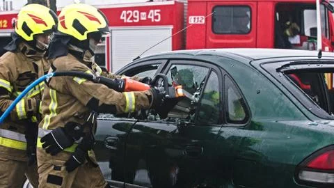 Firefighter beraking glass using jaws of life to extricate trapped victim from Stock Photos