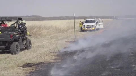 Firefighter dousing perimeter of controlled burn of prairie grass Stock Footage 268995541