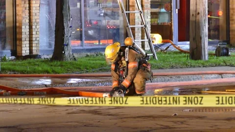 Firefighter emptying out fire hose in street behind emergency ribbon. Stock Footage 145984299