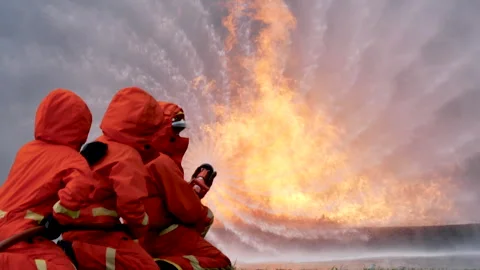 Firefighter fighting with flame using fire hose chemical water foam spray engin Stock Footage 254135893
