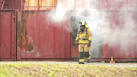 A firefighter in full protective gear runs out of a smoke-filled structure 스톡 동영상 326216915