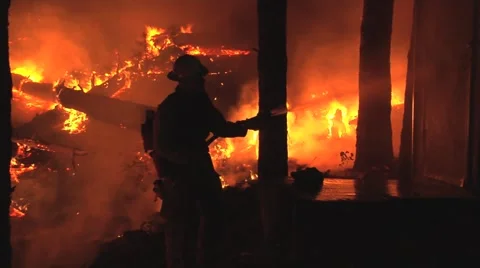 Firefighter hosing down outbuiliding at night and building fireline Stock Footage 40953650