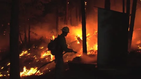 Firefighter hosing down outhouse to save it from the fire at night Stock Footage 40955311
