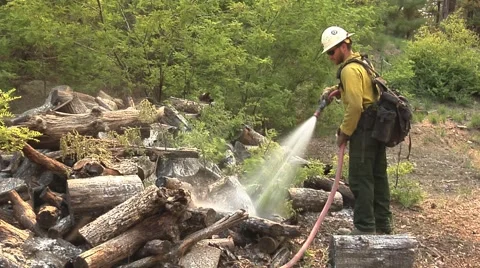Firefighter hosing down wood pile to prevent burning Stock Footage 40954225