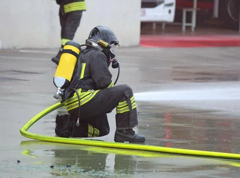 Firefighter kneeling to avoid flames with oxygen tank during fire station d.. Stock Photos