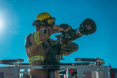 Firefighter on ladder next to lance to launch pressurized water. Stock Photos