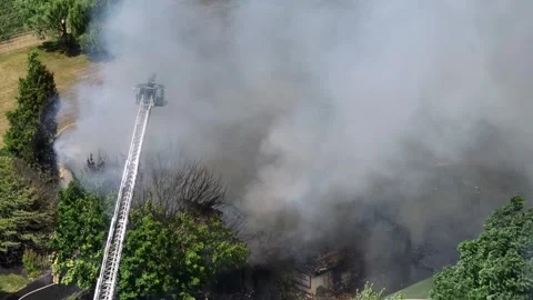 Firefighter on ladder spraying with water on burning farm house after Stock Footage 280027618