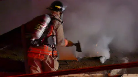 Firefighter On Ladder Uses Axe To Make Holes In Roof Video stock 65746778