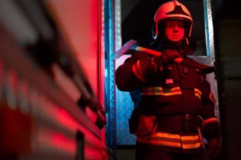 Firefighter man with hammer on his shoulder standing near fire engine Stock Photos