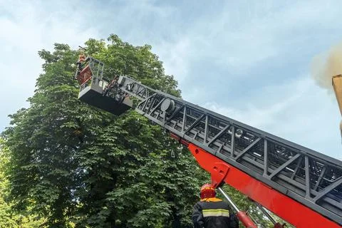 Firefighter operating hydraulic rescue platform ladder extended high in the.. 스톡 사진