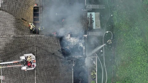 Firefighter spraying water with hose on burning house roof with ash. Aerial top Stock Footage 314354732