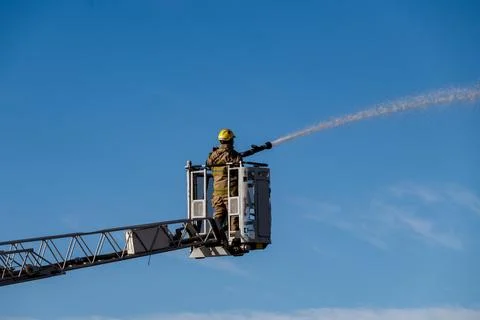 A firefighter is spraying water from a hose while standing on a ladder Stock Photos