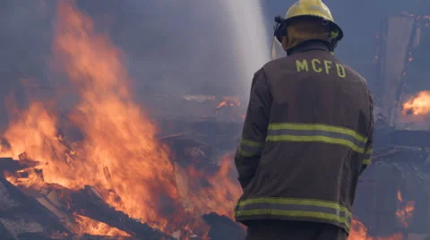 A firefighter sprays water on flames blazing above rubble from a house fire Stock Footage 59222381