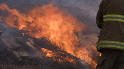 A firefighter sprays water on flames burning above a pile of rubble in the wake Stock Footage 59222338