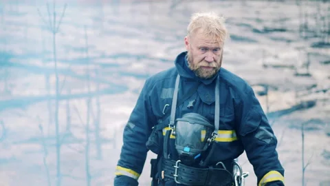 Firefighter is standing in the forest fire area and looks into the camera Video stock 166582994